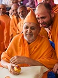 Swamishri sanctifies the decorated coconut and then tosses it back to the devotees