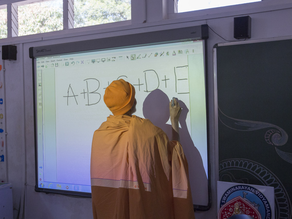 Param Pujya Mahant Swami Maharaj writes on a board in a class, 8 Mar 2017