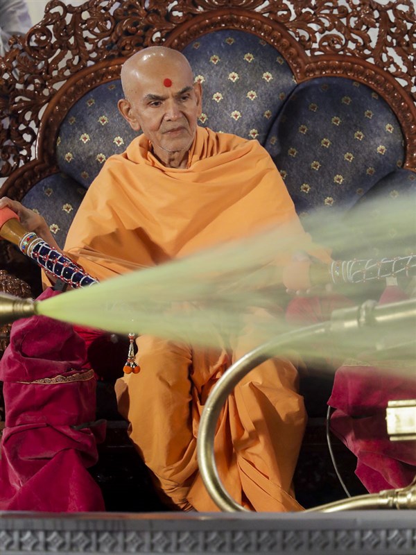 Param Pujya Mahant Swami Maharaj showers sanctified saffron-scented water on devotees
