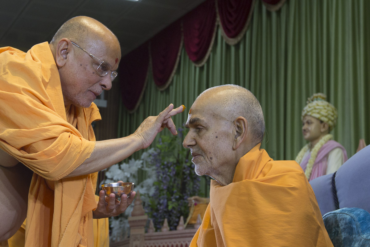 Pujya Ishwarcharan Swami applies chandlo to Swamishri, 16 Apr 2017