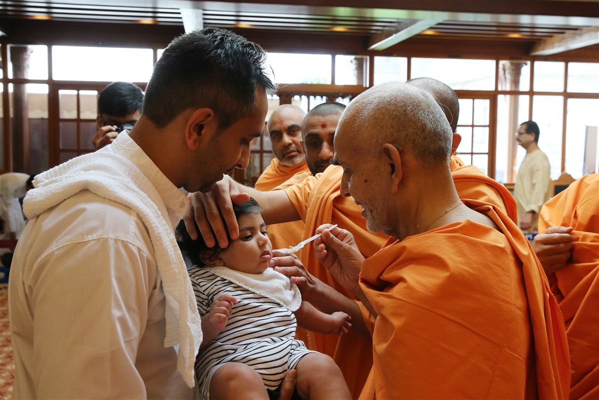 Swamishri performs annaprashan samskar to a young child