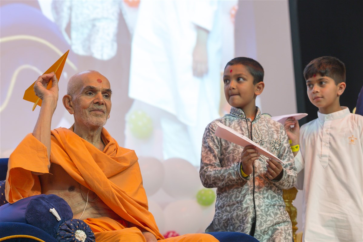 Swamishri flies a paper plane in the Bal-Balika Mandal shibir with other children