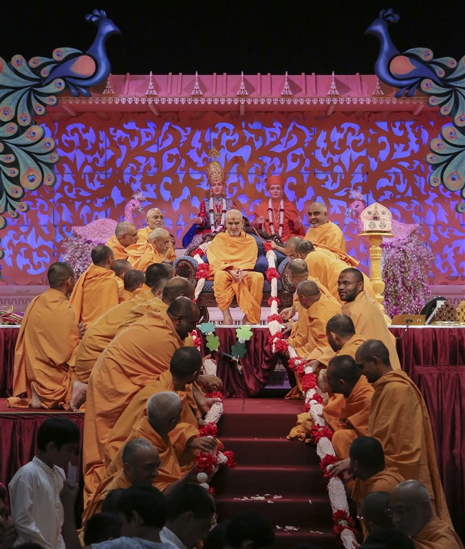 Sadhus honour Swamishri with a garland composed of rice puffs embellished with the 'Swaminarayan' mahamantra