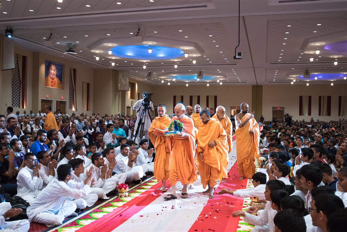 Youths offer flowers at Swamishri's feet as he arrives in the welcome assembly