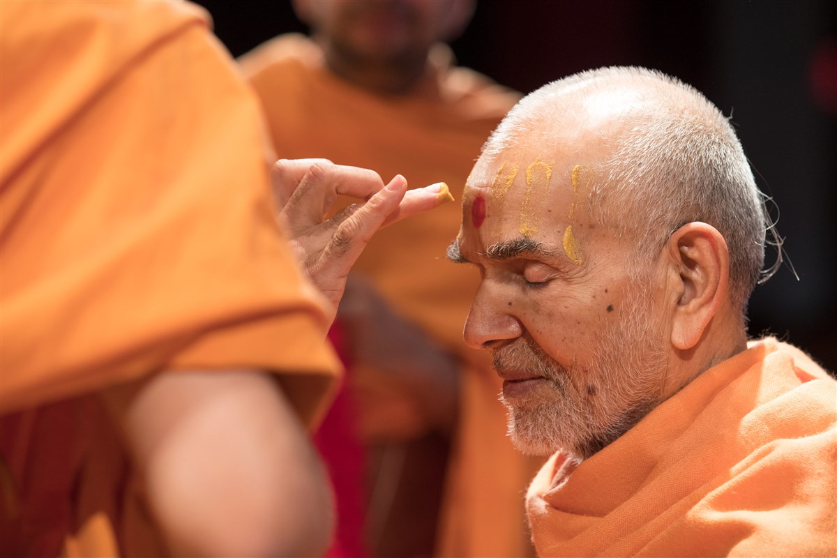 Swamis apply sandalwood to Swamishri's forehead as a welcoming gesture