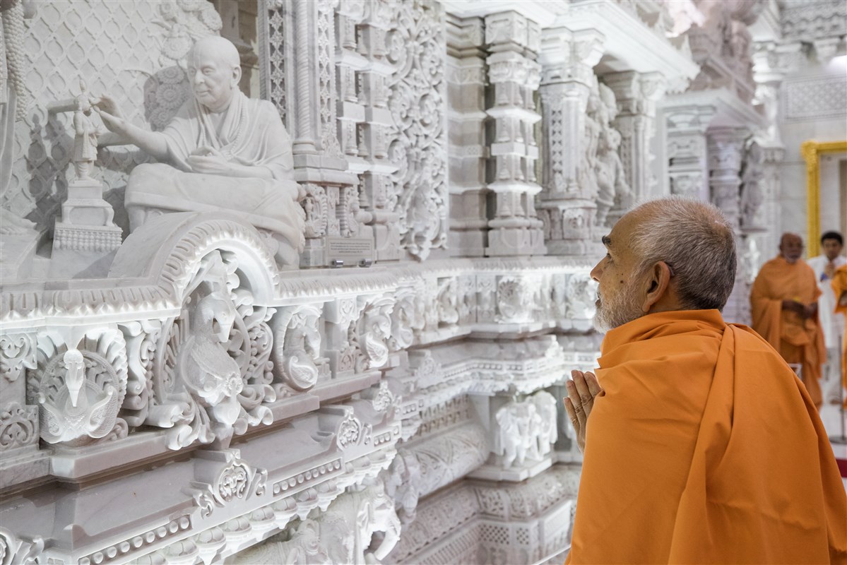 Swamishri engrossed in darshan of murti depicting consecration ceremony done by Pramukh Swami Maharaj