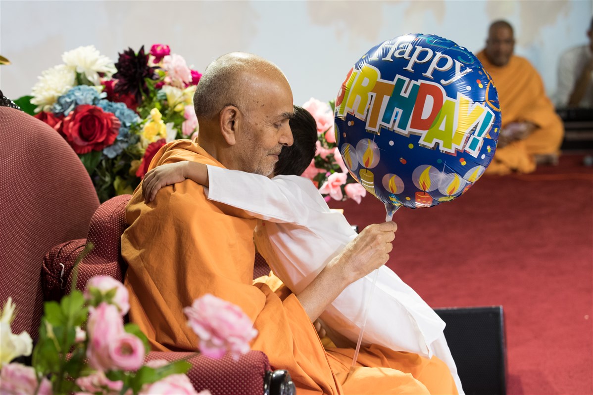 A child offers a balloon to Swamishri and hugs him