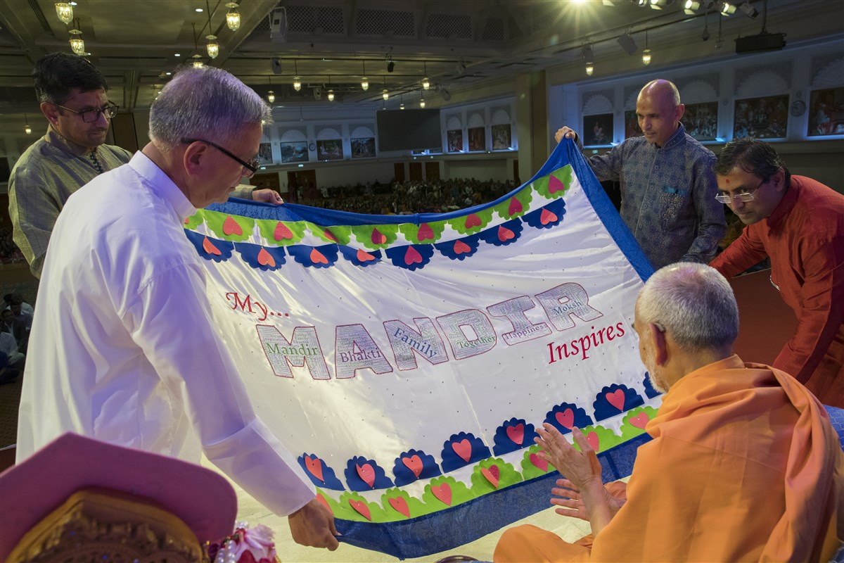 Devotees of East London present to Swamishri a decorative shawl with inspiring messages about their upcoming mandir