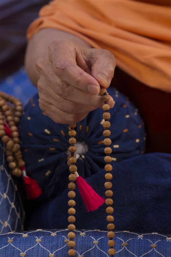 Swamishri rotates the mala as he listens to the presentations
