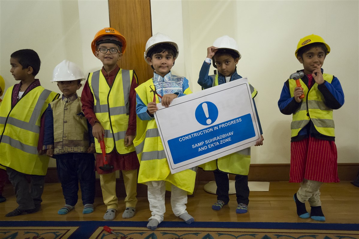 Children dressed as construction workers greet Swamishri with inspiring messages