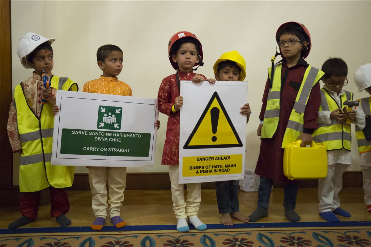 Children dressed as construction workers greet Swamishri with inspiring messages