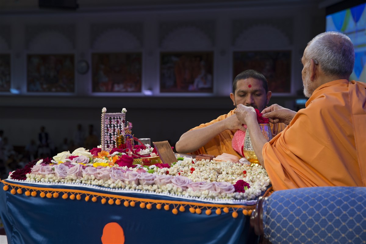 Swamishri sanctifies water with rose petals from his puja