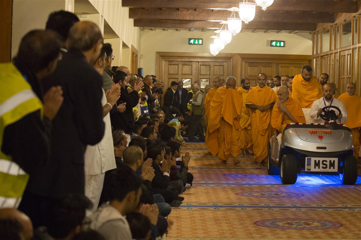 Swamishri proceeds to the assembly hall, greeting devotees with folded hands on his way
