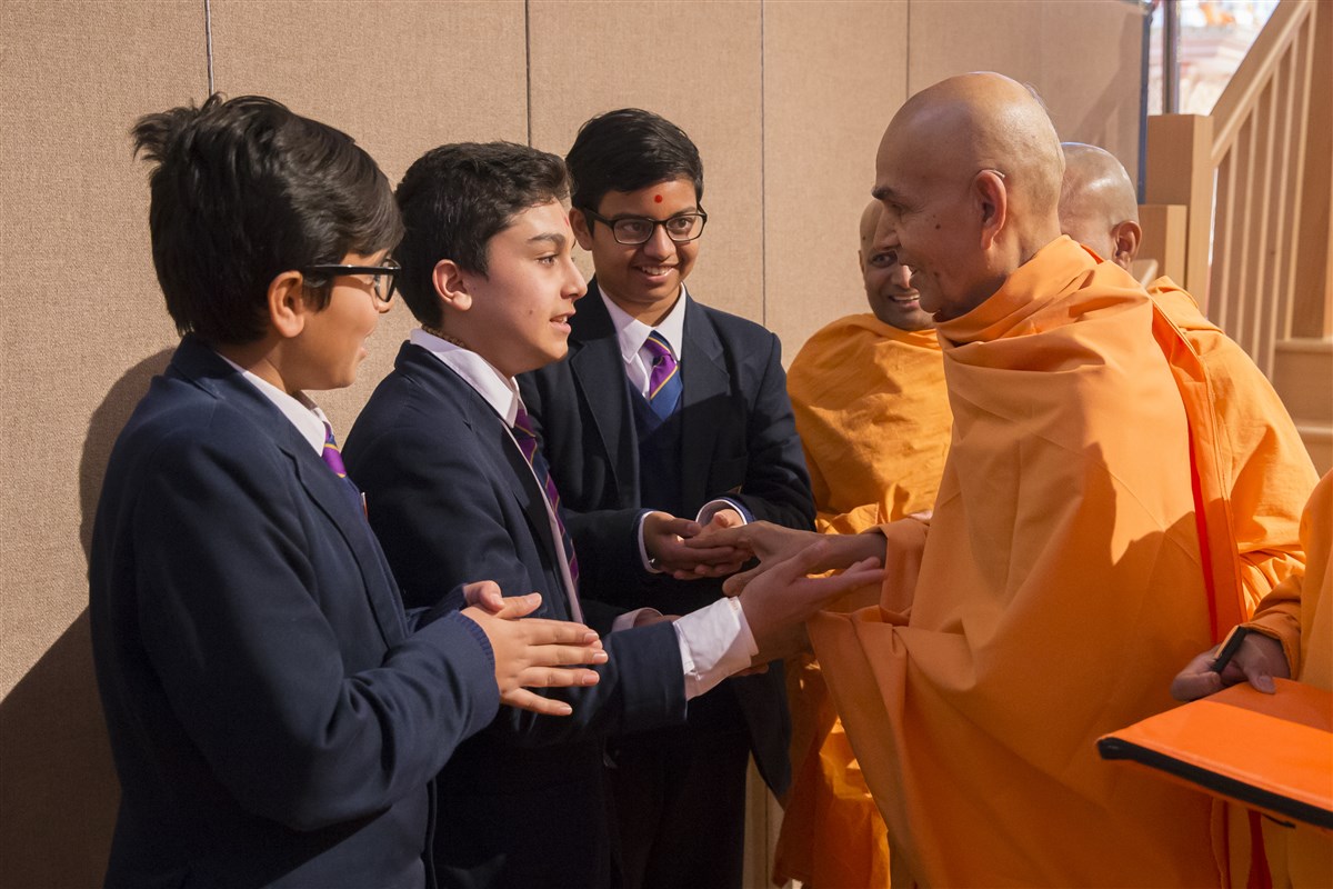 Swamishri engages with and blesses children as he departs the hall