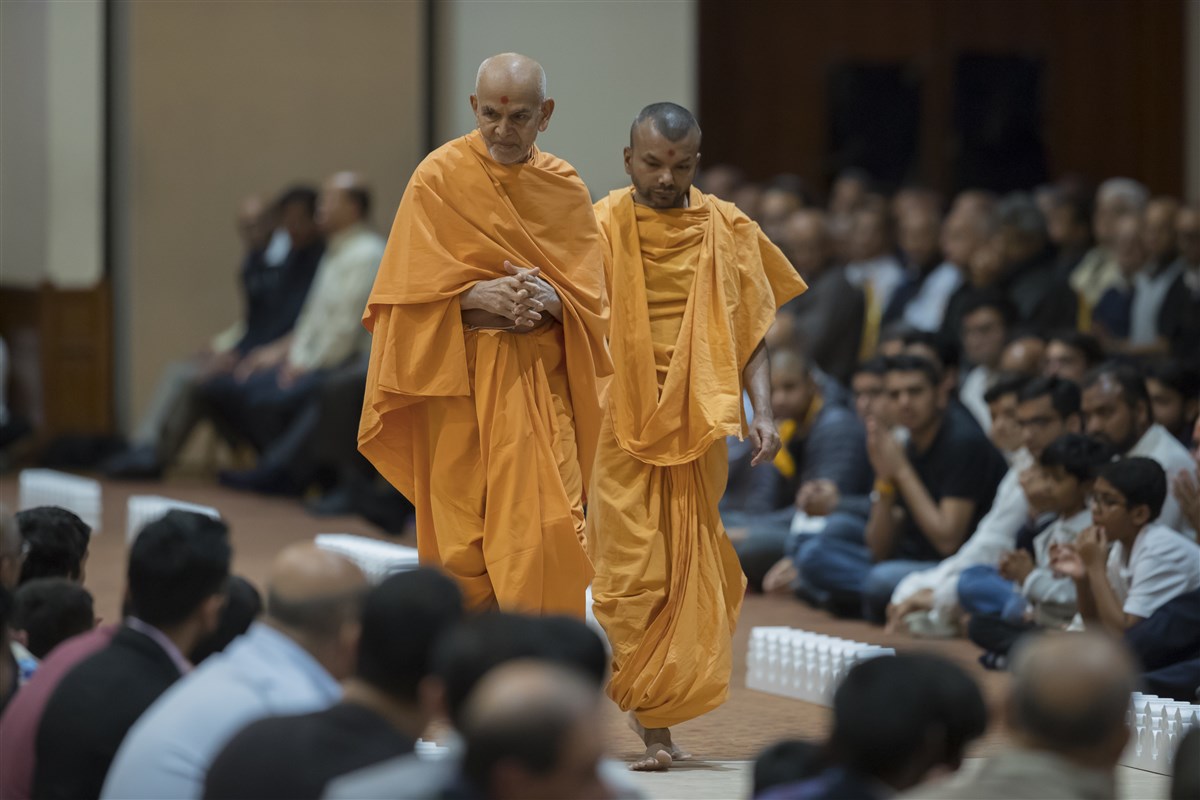 Swamishri looks on at devotees as he walks in the assembly hall