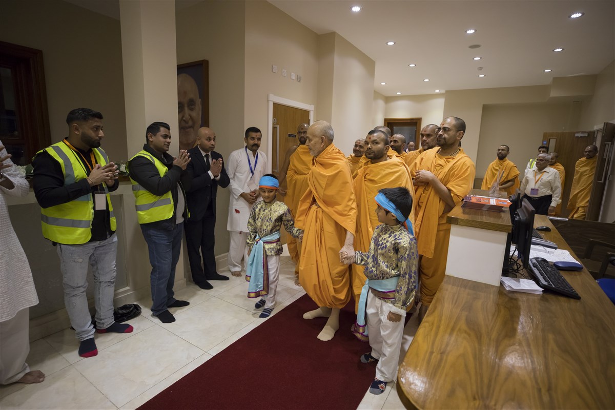 Param Pujya Mahant Swami Maharaj greets volunteers on his way to the abhishek mandap, led by two balaks