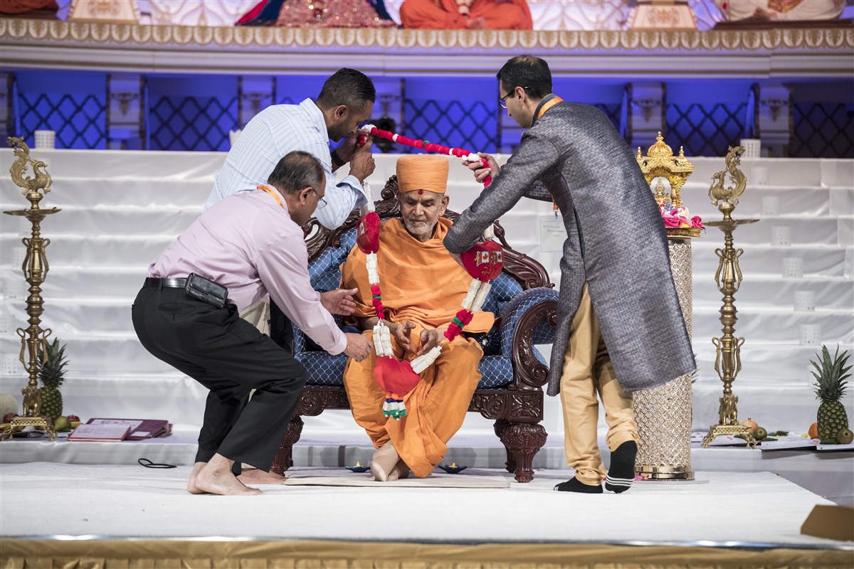 Devotees from around the world honour Swamishri with a decorative garland