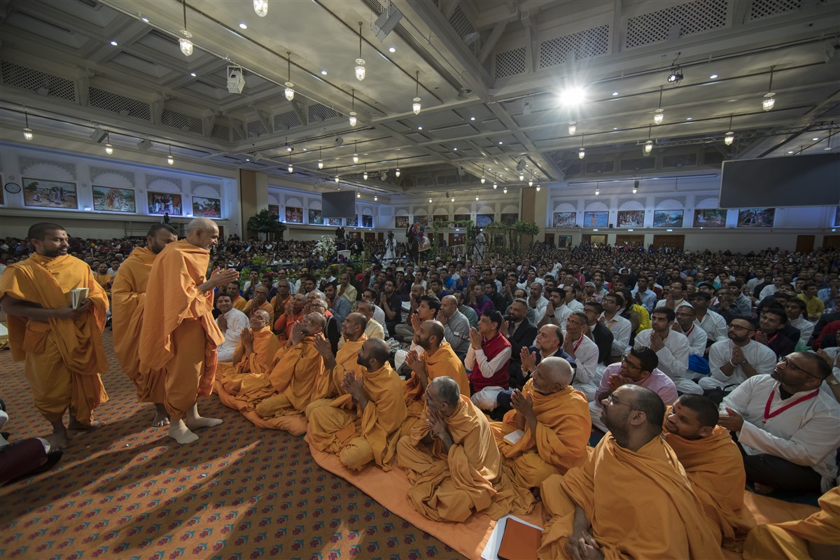 Swamishri departs the hall greeting devotees with folded hands
