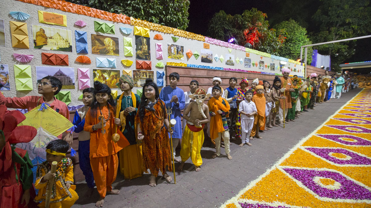 Children in traditional costumes welcome Swamishri