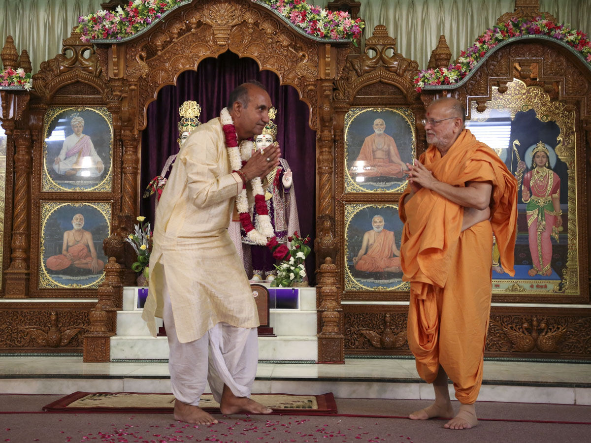 Pujya Ishwarcharan Swami honors Shri Ramkishore Tripathi, Honorary Professor, BAPS Swaminarayan Sanskrit Mahavidyalay, Sarangpur, with a garland