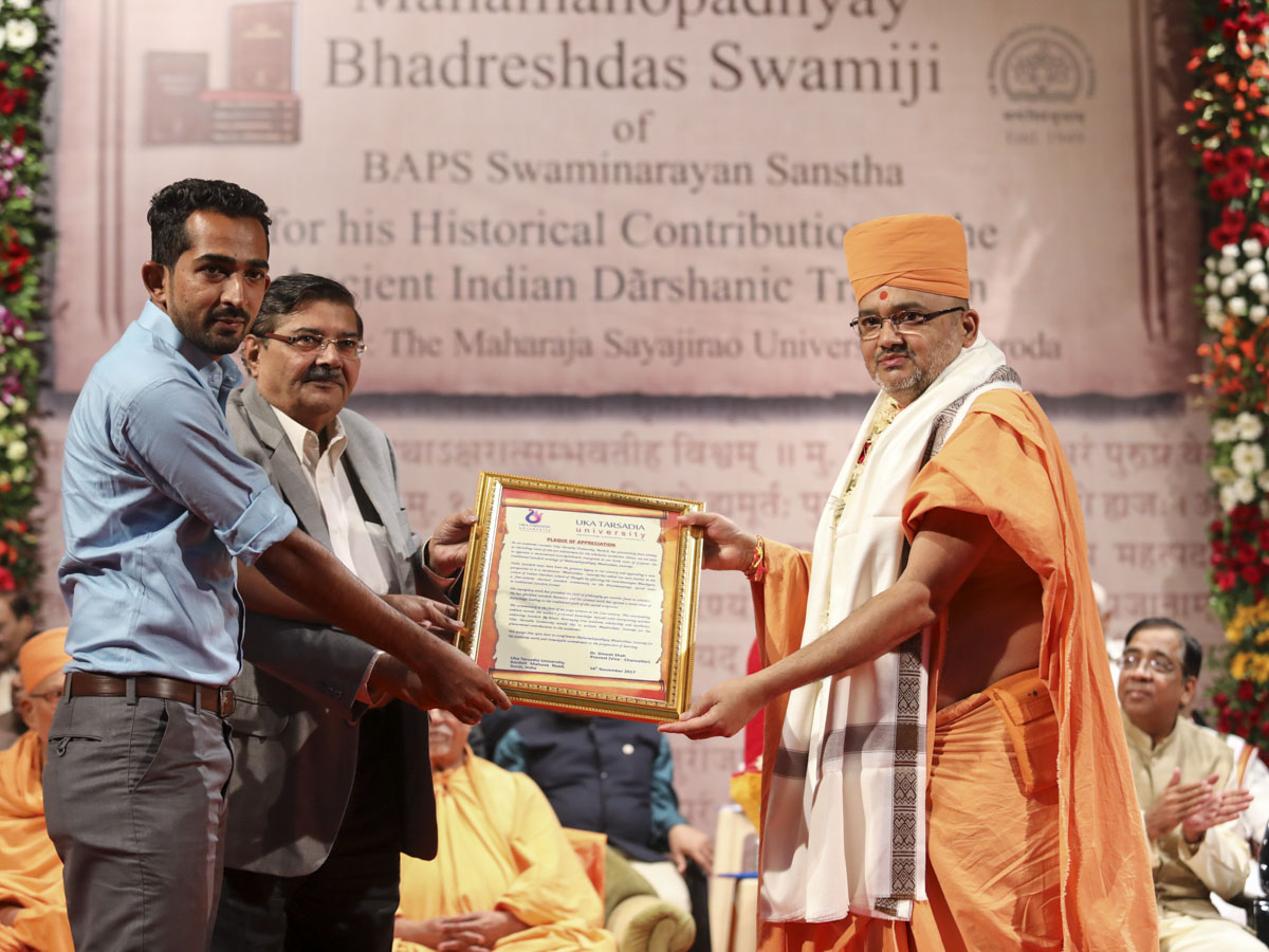 Dr. K. R. Desai and a representative of Uka Tarsadia University honor Bhadresh Swami