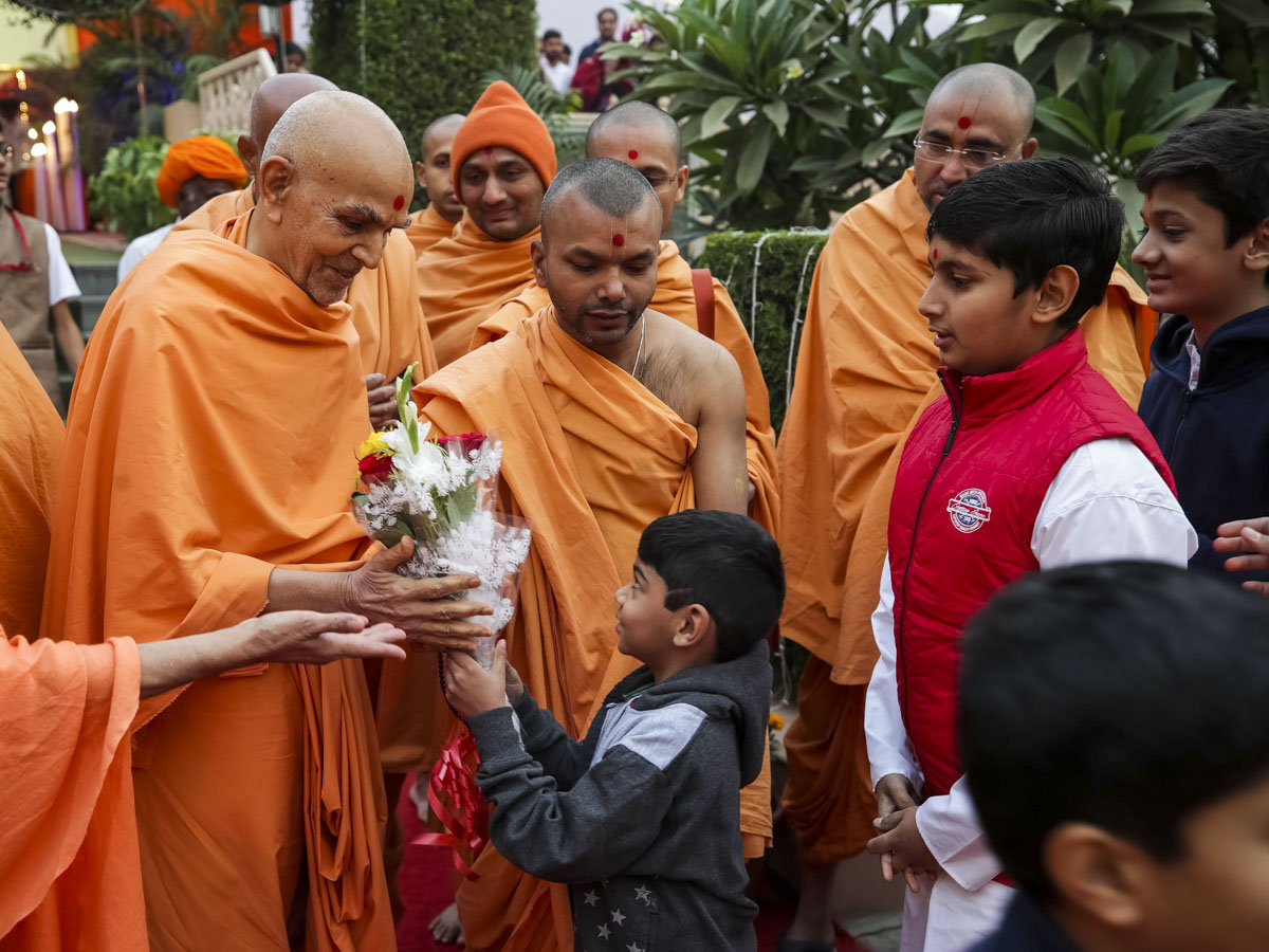 A child presents a bouquet to Swamishri