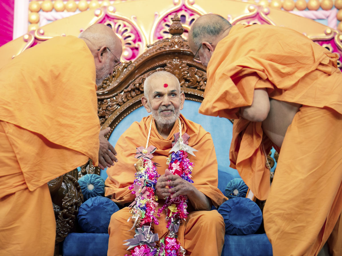 Pujya Ghanshyamcharan Swami and Pujya Ishwarcharan Swami honor Swamishri with a garland