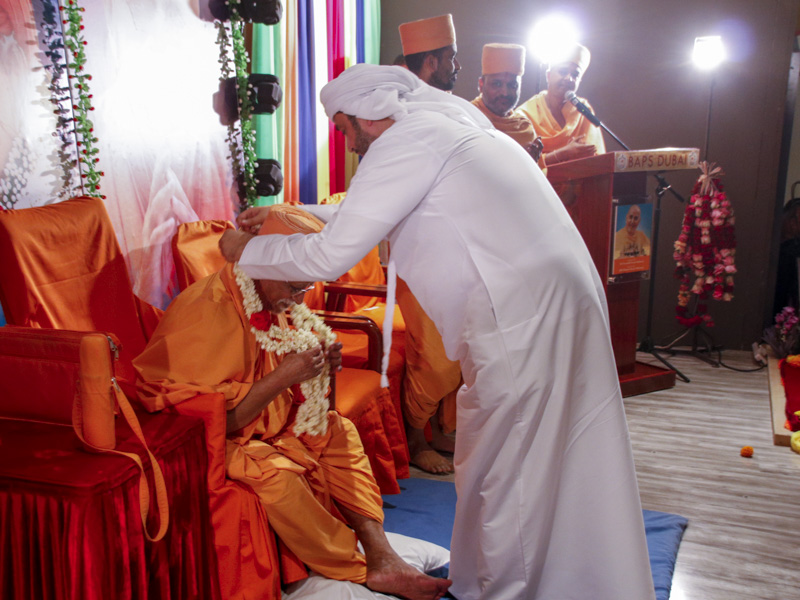 A guest honors Pujya Doctor Swami with a garland