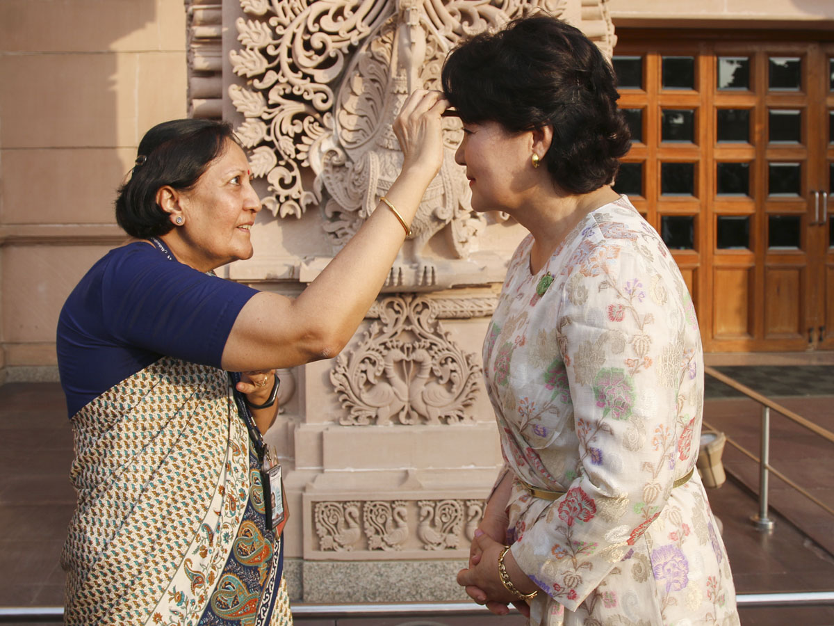 A senior volunteer welcomes First Lady Kim Jung-sook in a traditional manner to Swaminarayan Akshardham by applying a tilaka
