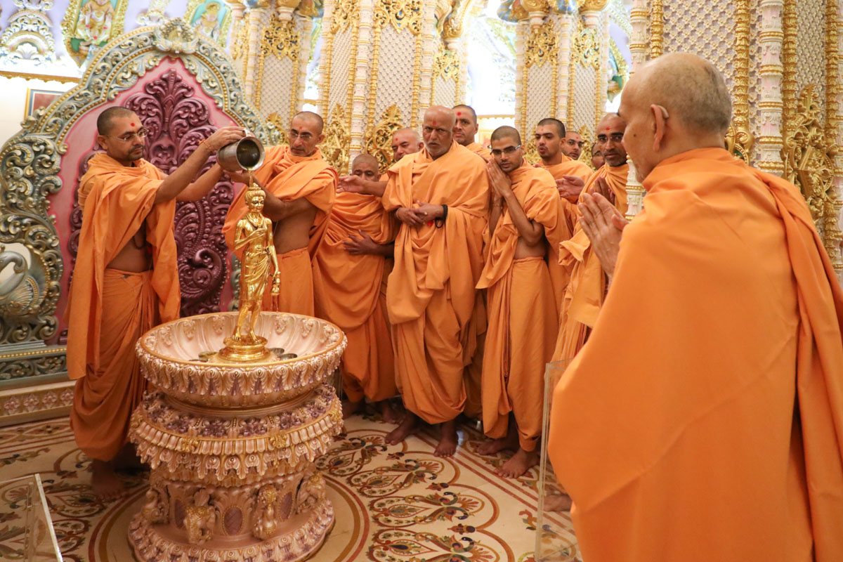 Swamishri engrossed in darshan while sadhus perform abhishek of Shri Nilkanth Varni