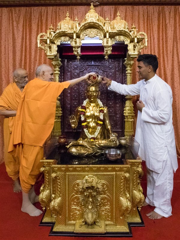 Swamishri and a devotee perform abhishek of Bhagwan Swaminarayan