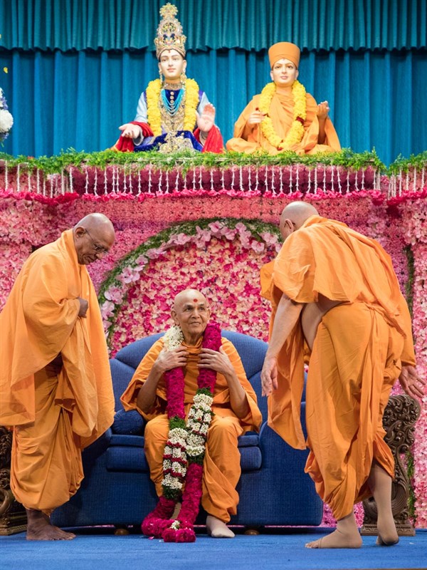Pujya Swayamprakash Swami (Doctor Swami) and Pujya Ishwarcharan Swami honor Swamishri with a garland