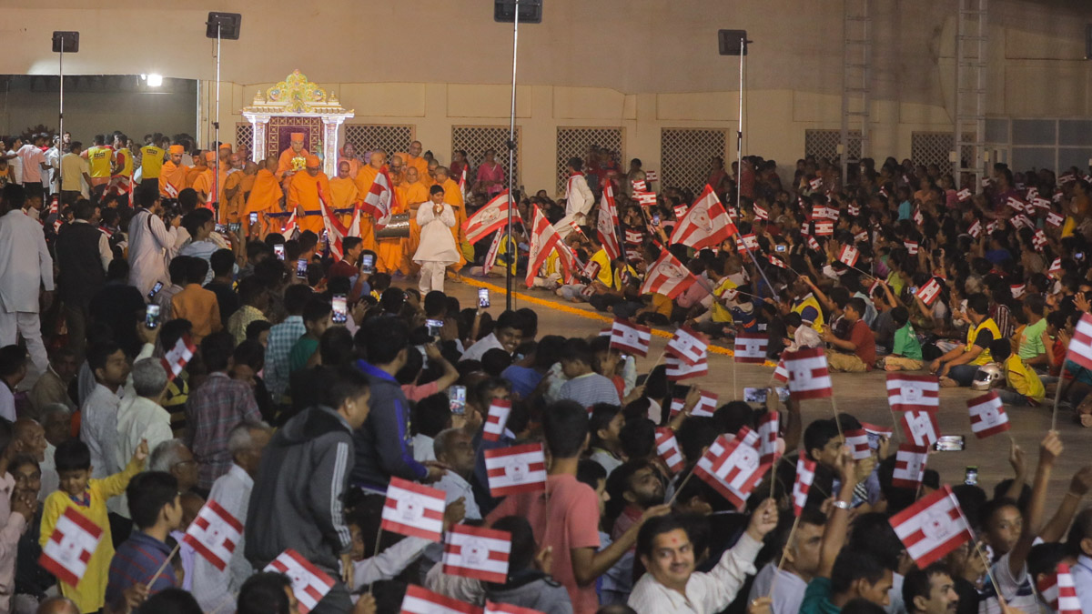 Devotees wave flags to welcome Swamishri in the evening satsang assembly
