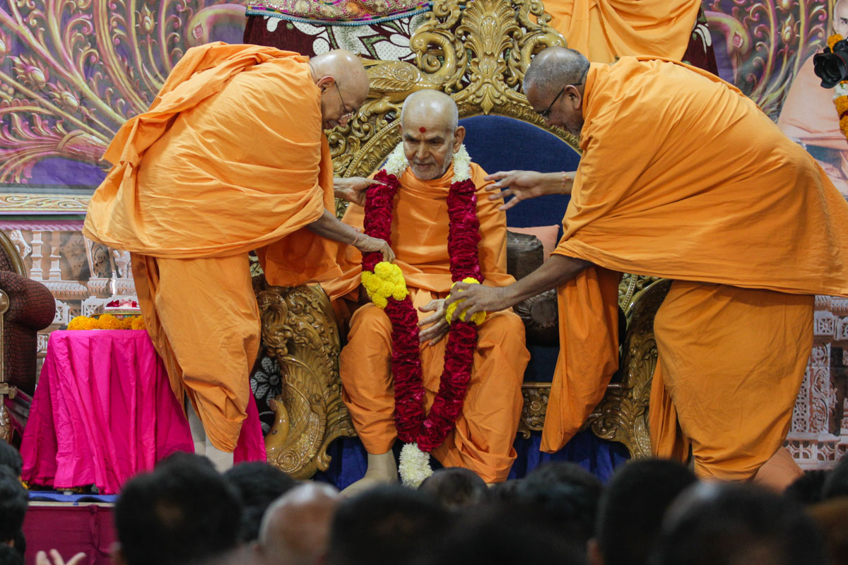 Pujya Tyagvallabh Swami and Vedagna Swami honor Swamishri with a garland