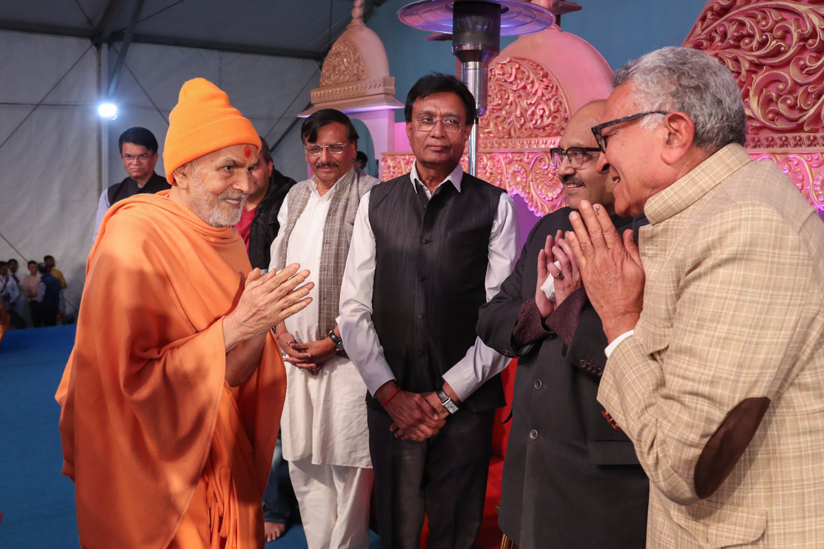 Swamishri greets invited guests on stage in the evening satsang assembly