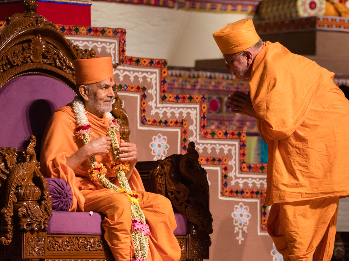 Pujya Ishwarcharan Swami honors Swamishri with a garland