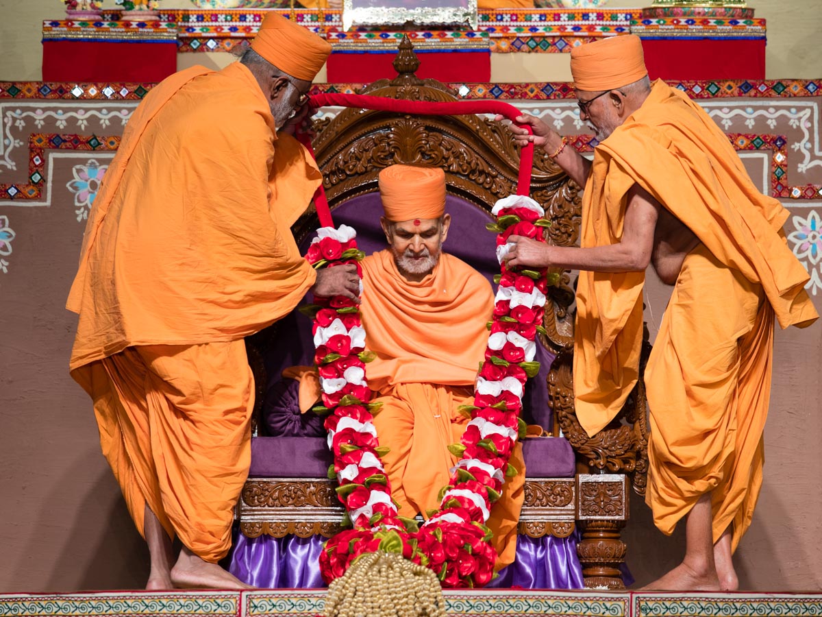 Pujya Kothari Swami and Abhayswarup Swami honor Swamishri with a garland