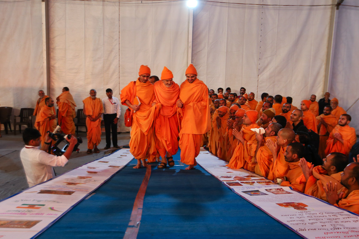 Param Pujya Mahant Swami Maharaj observes birthday cards prepared by devotees in honor of Brahmaswarup Pramukh Swami Maharaj's 98th birthday celebration