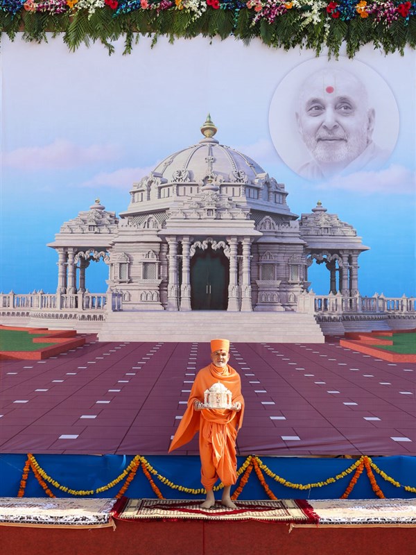 Swamishri standing with Shri Harikrishna Maharaj in front of a banner of Pramukh Swami Maharaj's Smruti Mandir