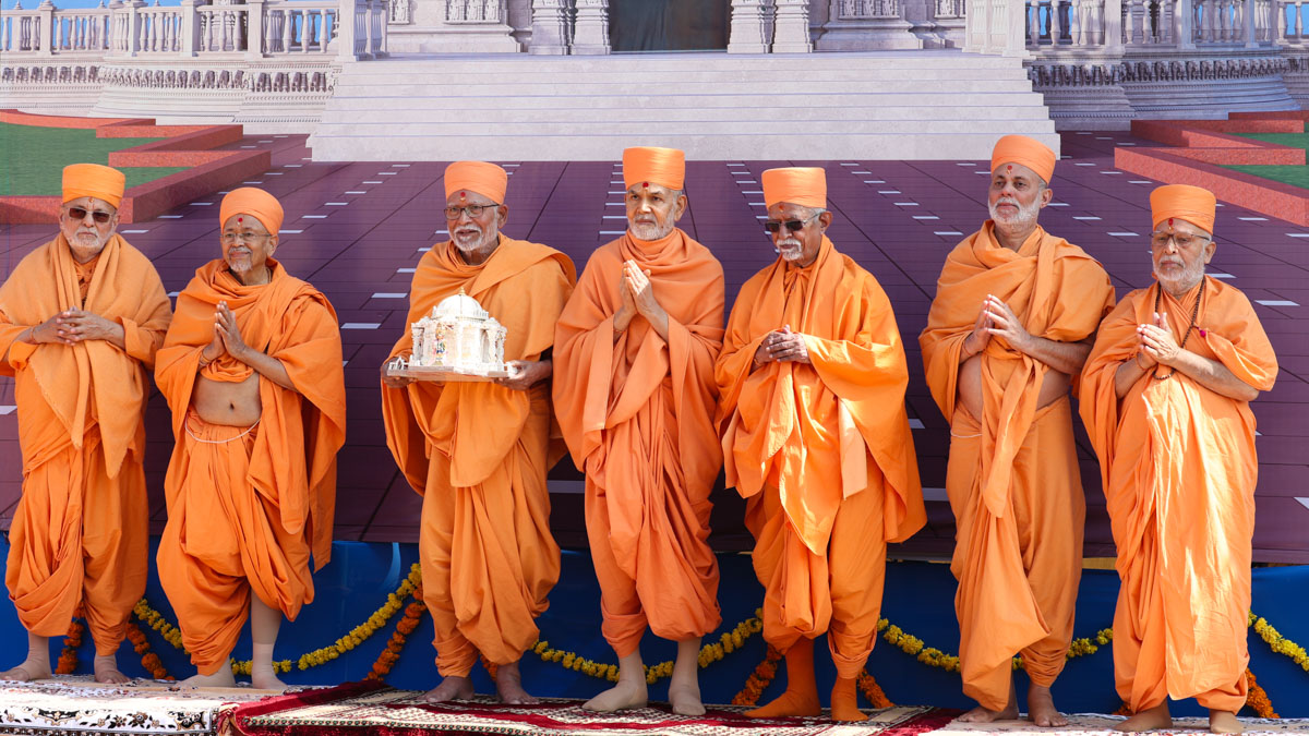 Swamishri and senior sadhus with Shri Harikrishna Maharaj in front of a banner of Pramukh Swami Maharaj's Smruti Mandir