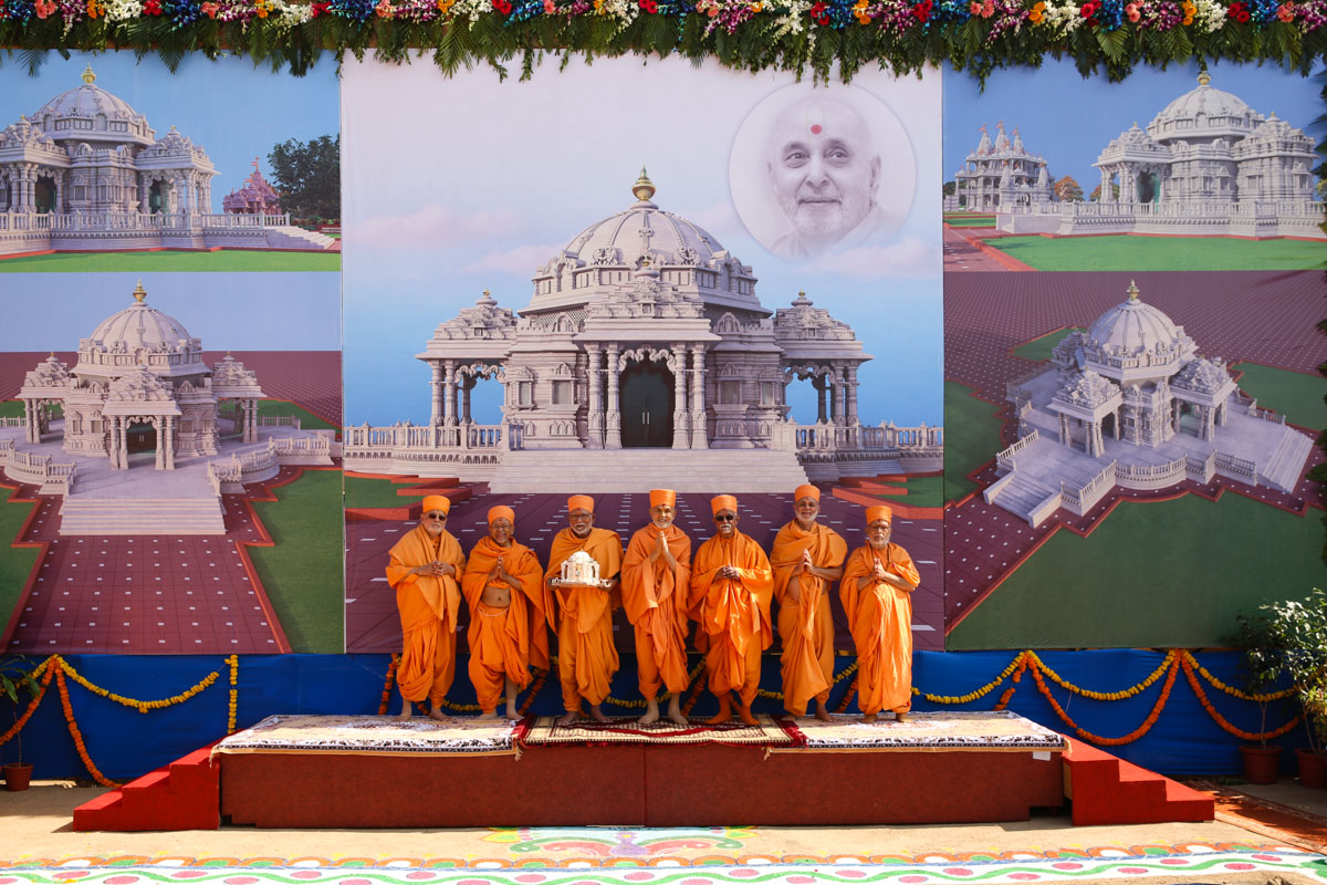 Swamishri and senior sadhus with Shri Harikrishna Maharaj in front of a banner of Pramukh Swami Maharaj's Smruti Mandir