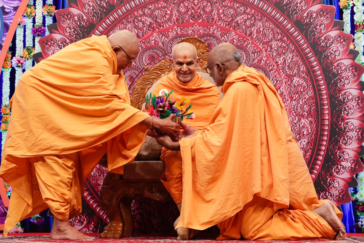 Pujya Kothari Swami and Abhayswarup Swami present a flower bouquet to Swamishri