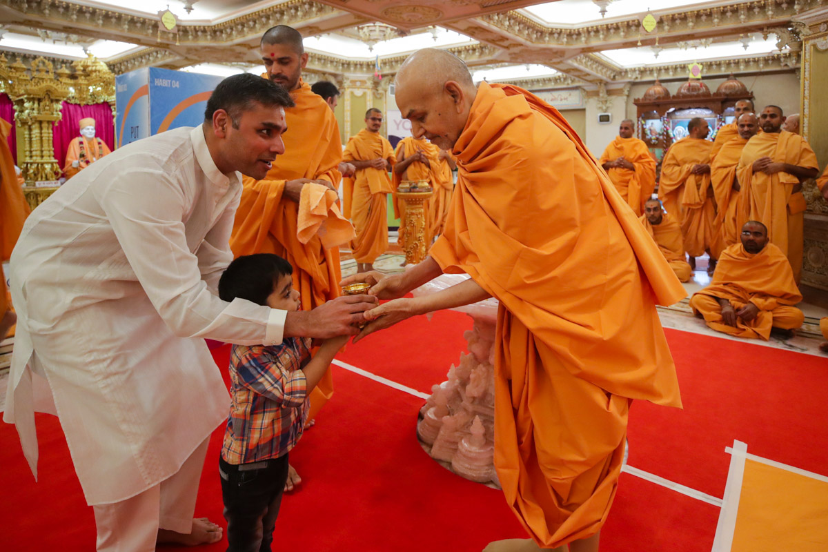 A child presents Swamishri a kalash for abhishek