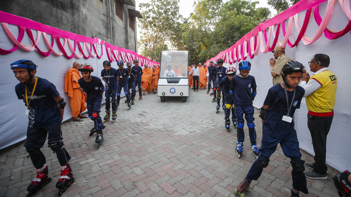 Students on roller skates lead Swamishri to the mandir