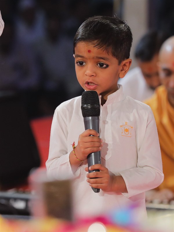A child presents mukhpath before Swamishri