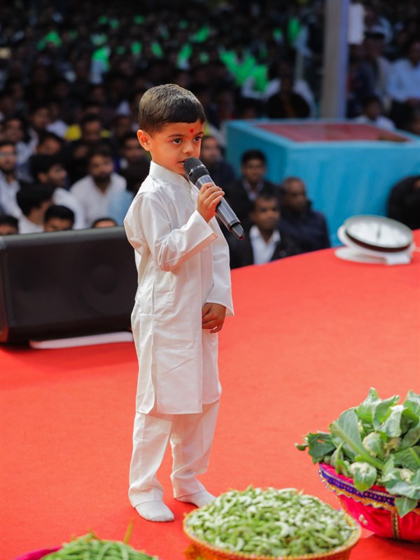 A child presents mukhpath before Swamishri