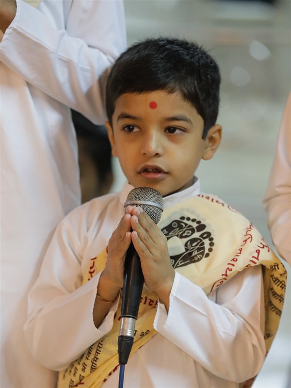 A child sings shloks while Swamishri performs abhishek
