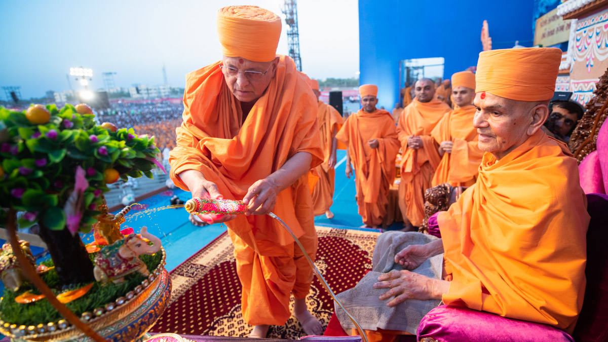 Pujya Ishwarcharan Swami sprays saffron-scented water on Shri Harikrishna Maharaj