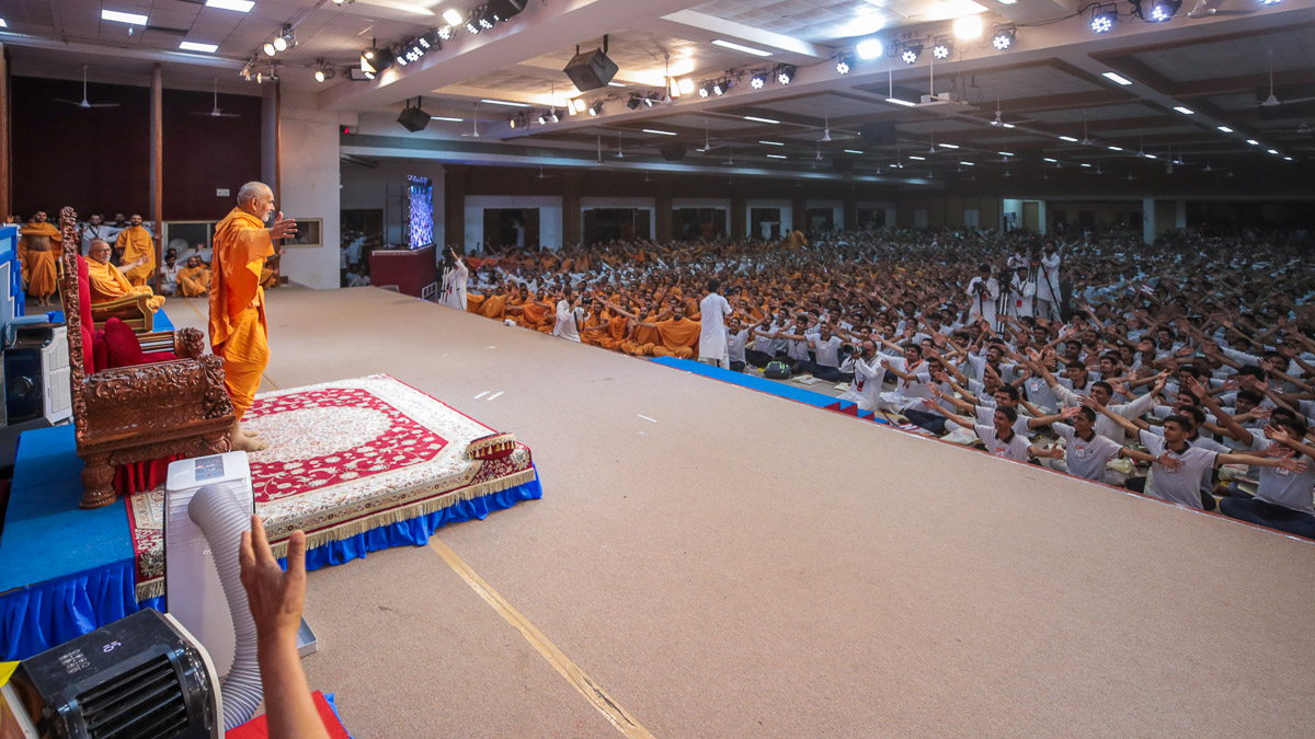 Swamishri and youths gesture to embrace each other
