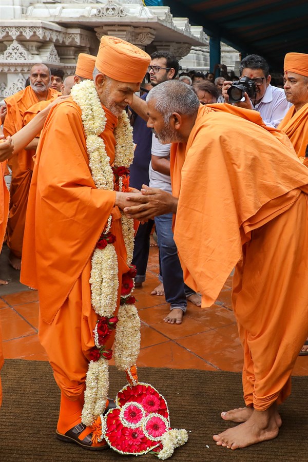 Atmakirti Swami honors Swamishri with a garland before he departs